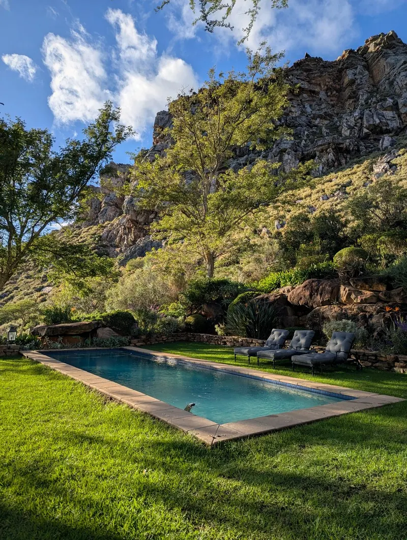 A pool on a green lawn below a mountain